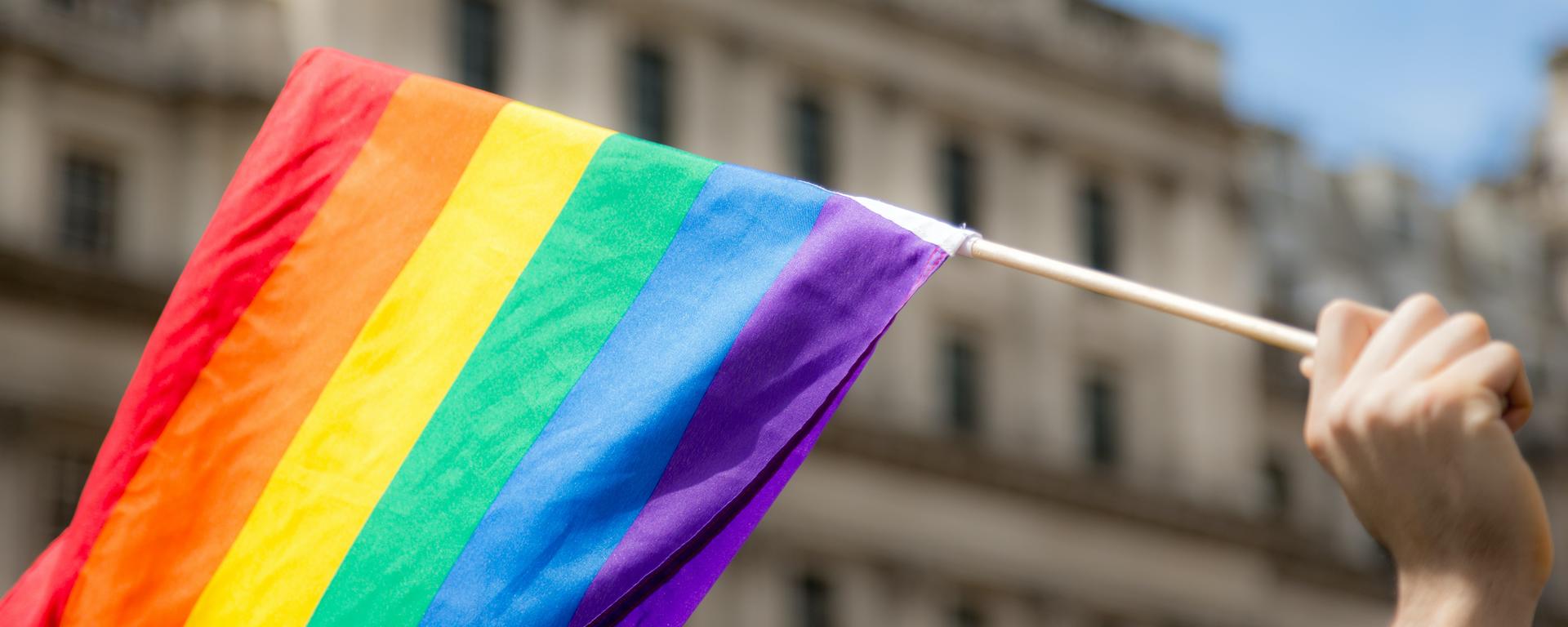 A hand holds a Pride flag