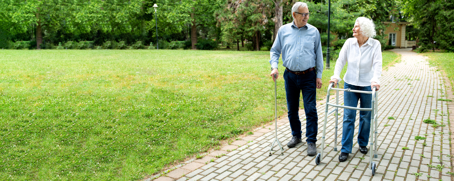 Senior man using a walking cane accompanied by a senior lady strolling with folding walker