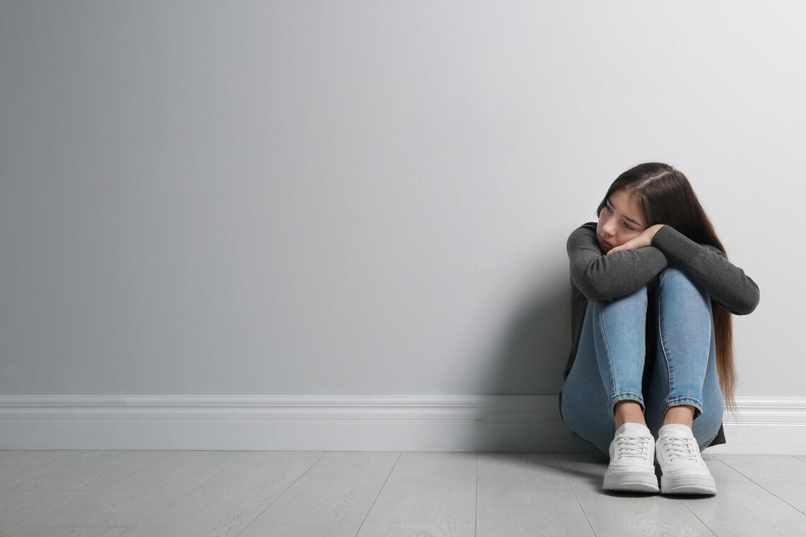 Sad youth sits next to a blank wall 