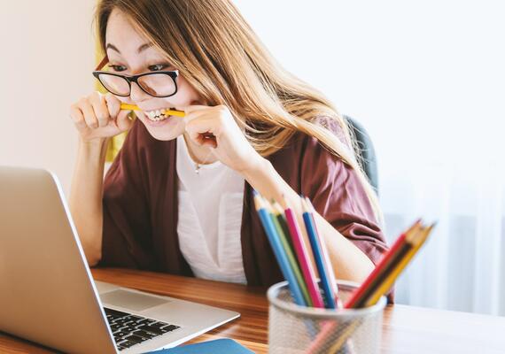 student bites her pencil in frustration while working on a laptop